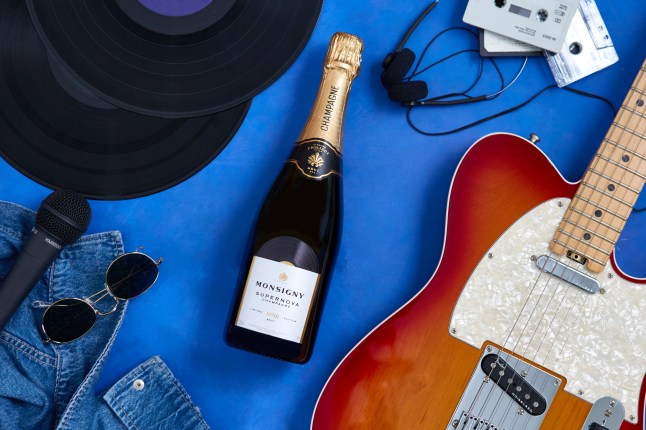 Aldi's limited edition Supernova version of the Veuve Monsigny champagne brut on a flat lay with a guitar and glasses, casette tapes and other musical items