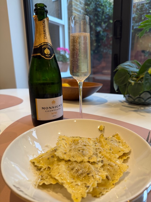 The Aldi champagne bottle and a flute on a table with a bowl of pasta