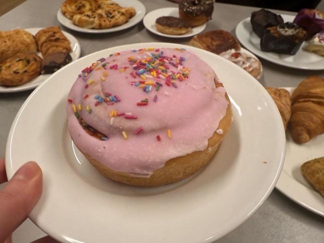 Lidl's Birthday Cake Bun on a plate, with other baked goods in the background