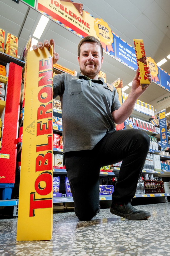 A Morrisons employee holding a regular Toblerone and the giant one to show size