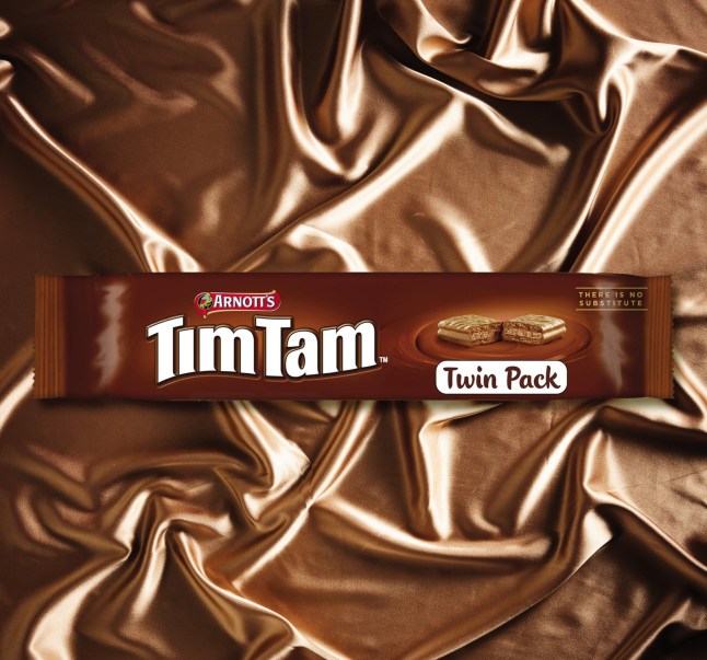 A twin pack of Tim Tam biscuits against a backdrop of brown silky material.